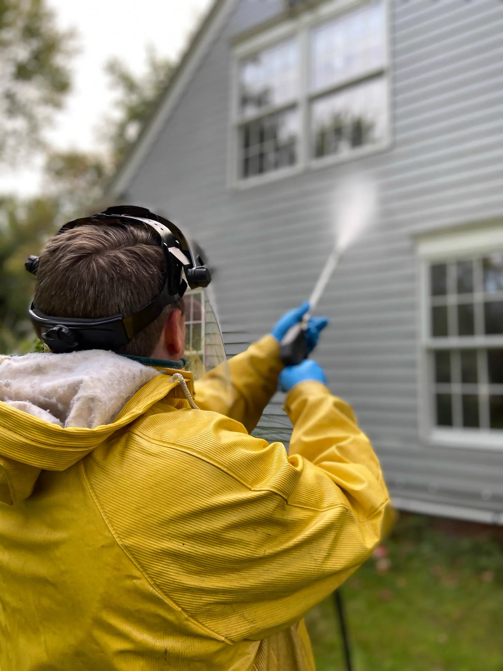 Technician in protective gear pressure washing the vinyl siding of a house