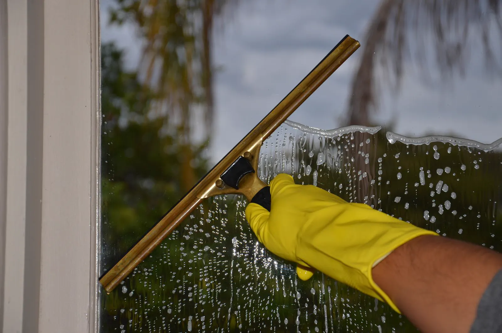 Gloved hand pulling a brass squeegee across a soapy window